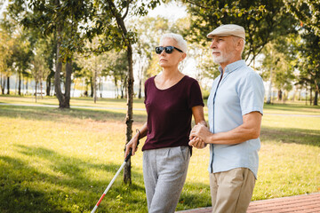 Elderly couple walking in the park. Senior woman is blind holding stick old man helping her to walking. Mature supposes spending time in nature enjoying outdoors retirement medicine concept copy space