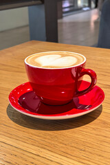 Coffee with heart pattern in bright red cup standing on wooden table in cafe