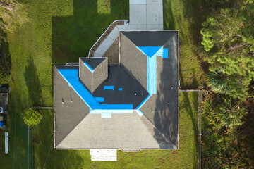Aerial view of damaged in hurricane Ian house roof covered with blue protective tarp against rain...