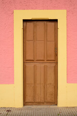 Puerta de madera en pared rosa y marco amarillo