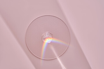 A drop of serum on a round stand on a pink background with beautiful caustics.