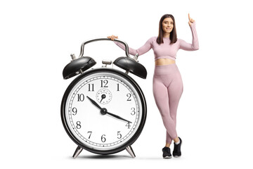 Young fit woman in sportswear with alarm clock pointing up