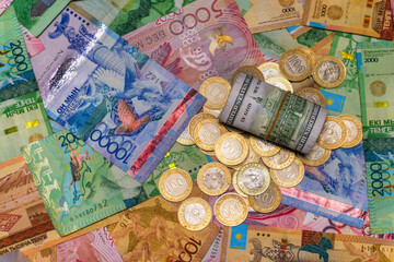 A folded $100 bill lies on top of coins and tenge bills