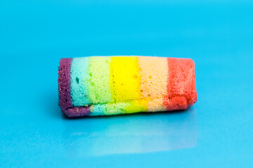 Vibrant rainbow colored sponge cake roll on a bright blue surface