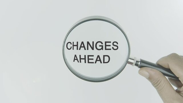 "Changes Ahead" text or word highlighted by a magnifying glass in a hand on a white background, symbolizing transformation, evolution, and progress