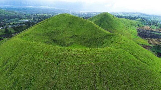 aerial view of green hills peak with grassland and mountain views of Wurung Crater, Indonesia. Aerial shot of the green grassy peak of the mountain crater.