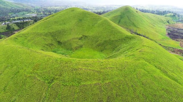 aerial view of green hills peak with grassland and mountain views of Wurung Crater, Indonesia. Aerial shot of the green grassy peak of the mountain crater.