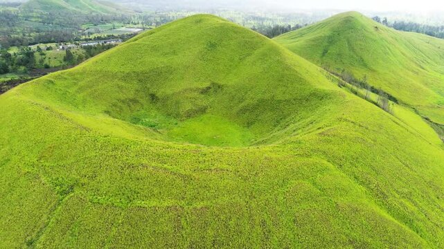 aerial view of green hills peak with grassland and mountain views of Wurung Crater, Indonesia. Aerial shot of the green grassy peak of the mountain crater.