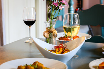 A table with a white bowl of food, a wine glass, and a vase of flowers