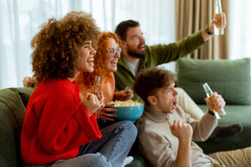 Friends cheer together while watching a thrilling sports match in a cozy living room on a sunny...