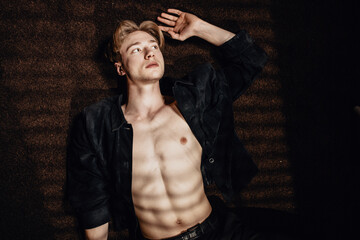 handsome man lies on the floor with an open shirt, revealing his six-pack, while looking up in thought, contemplating love, seduction, and sexy thoughts with hand to head