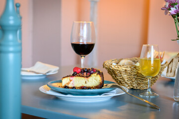 A plate of cheesecake with a glass of red wine and a glass of orange juice