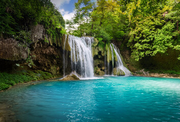 Nature’s masterpiece: a serene forest embracing a mesmerizing azure waterfall, where tranquility meets breathtaking beauty