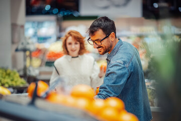 Happy couple choosing oranges in supermarket produce section