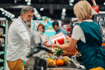 Senior customer paying for groceries at supermarket checkout counter