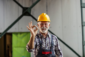 Portrait of senior industry worker standing in facility and gesturing okay at the camera.