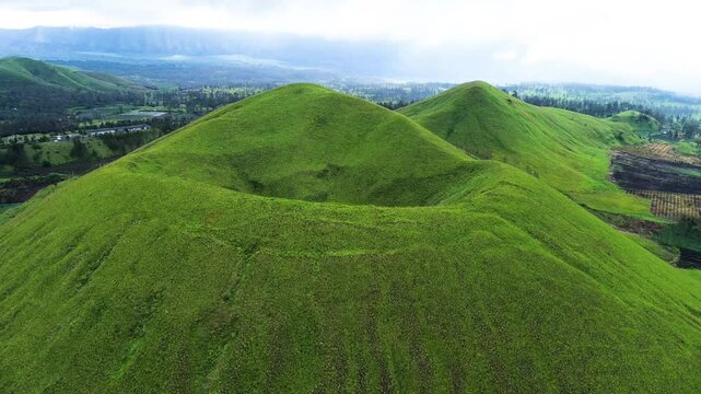 aerial view of green hills peak with grassland and mountain views of Wurung Crater, Indonesia. Aerial shot of the green grassy peak of the mountain crater.