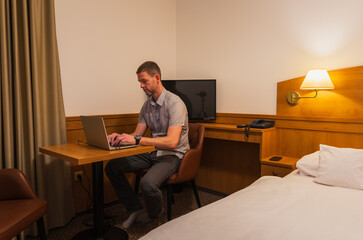 A man sits on a chair in a hotel room and works, relax on his laptop, searching the internet