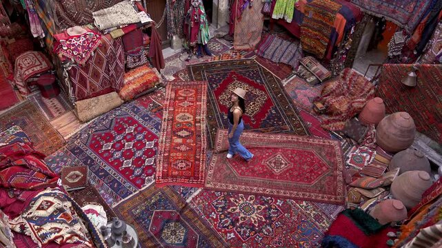 A photographer tourist browses handmade carpets and kilims in a shop, capturing the intricate designs with a camera. Authentic carpets hang wall, reflecting the rich culture of Cappadocia, Turkey.