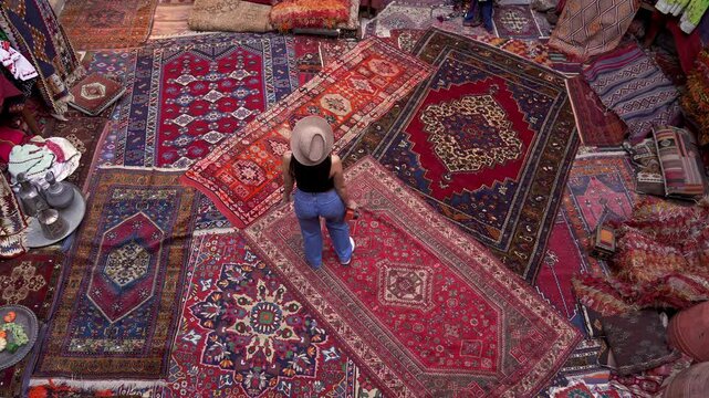 A photographer tourist browses handmade carpets and kilims in a shop, capturing the intricate designs with a camera. Authentic carpets hang wall, reflecting the rich culture of Cappadocia, Turkey.