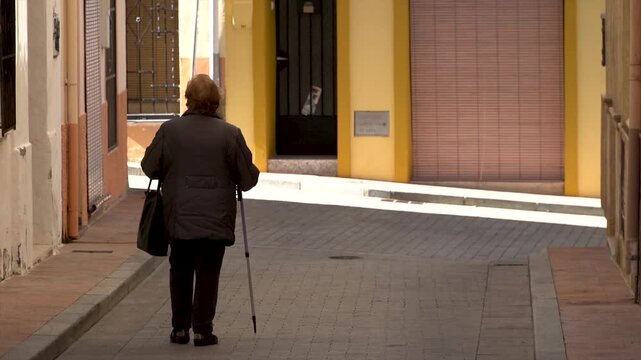 Slow motion, elderly woman walking with a hicking stick in the street.