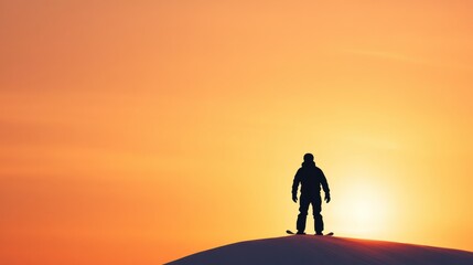 Fototapeta premium Silhouette of a snowboarder standing on a snow-covered hill against a vibrant sunset sky
