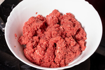 Fresh ground meat in a bowl with a coarse reddish texture, ideal for preparing homemade dishes like...