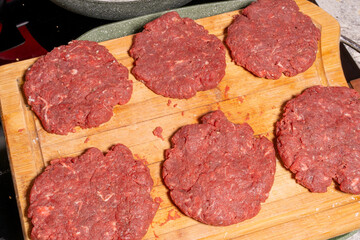 Uncooked burger patties on a wooden cutting board with hamburger buns being toasted in the background. Perfect for BBQ or homemade cooking scenes.