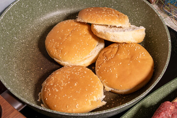 Toasted sesame seed buns arranged in a frying pan, showcasing the preparation of fresh bread for burgers or sandwiches in a homey style.
