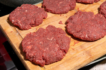 Fresh, raw hamburger patties on a wooden cutting board, ready for cooking. The texture and arrangement highlight the simplicity of burger preparation.