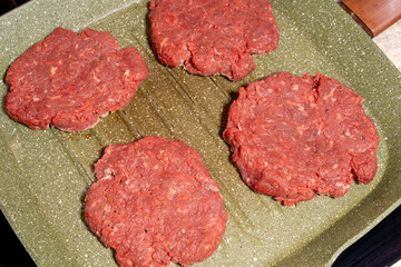 Four raw hamburger patties of ground beef on a ridged green grill pan, perfect for grilling or frying as part of homemade burger preparation.