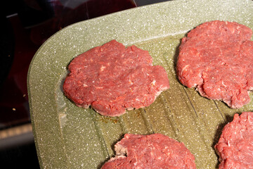 Four raw hamburger patties of ground beef on a ridged green grill pan, perfect for grilling or frying as part of homemade burger preparation.