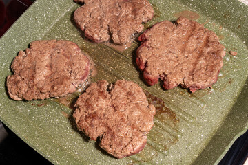 Four sizzling hamburger patties cook on a green griddle, showing texture, grease, and browning. A snapshot of burger preparation at its finest.