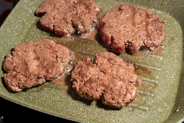 Four sizzling hamburger patties cook on a green griddle, showing texture, grease, and browning. A snapshot of burger preparation at its finest.