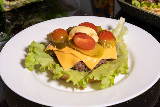An open-faced cheeseburger on a white plate with lettuce, tomato, pickles, and mayonnaise. A bright, fresh take on a classic meal.