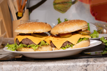 Two cheeseburgers with sesame buns, beef patties, melted cheddar, lettuce, pickles, and tomato sit...