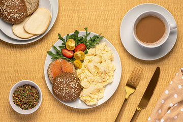 Food photography of keto breakfast with scrambled eggs and sandwich with low carb bun with smoked salmon tomato, arugula, smoked cheese scamorza and coffee cappuccino