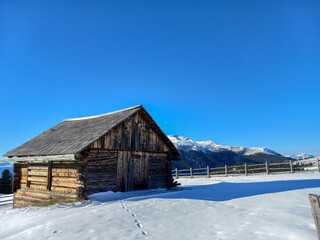 old wooden house in the snowy mountains with a wooden fence and Alps in the background of the ski cabin with a blue sky on a sunny day in the winter