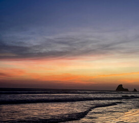 sunset on the beach in Nicaragua with a rock that looks like a shark tooth 
