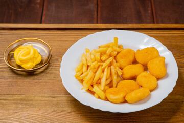 French fries and golden nuggets with cheese sauce on a small wooden table