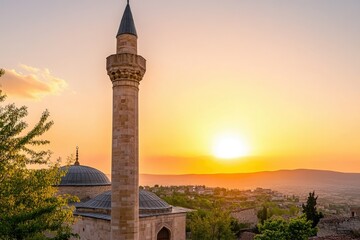 A majestic mosque minaret stands tall against a vibrant sunset, overlooking a picturesque town.