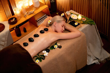 Hot stone massage at spa salon in luxury resort with warm candle light, blissful woman customer...