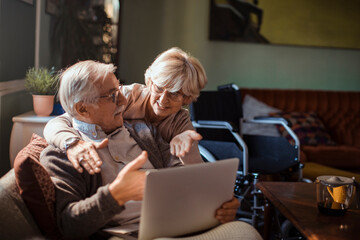 Elderly couple embracing while using laptop at home