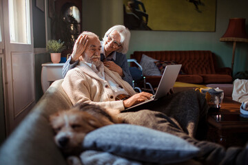 Elderly couple embracing while using laptop at home