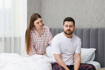Young woman comforting her resentful boyfriend on bed at home