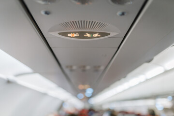 Illuminated no smoking and fasten seatbelt signs inside an airplane cabin. The safety indicators are displayed on the overhead passenger panel..