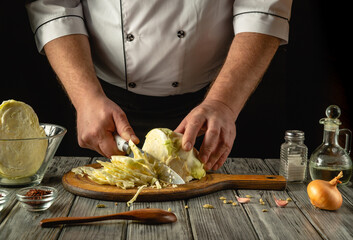 A chef dressed in a white uniform meticulously slices fresh cabbage on a rustic wooden board. Nearby ingredients like onions, oil, and spices create an inviting atmosphere in the kitchen