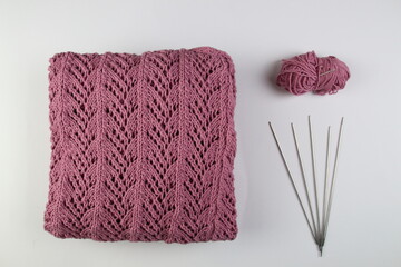 A pink handmade knitted sweater lies on a white background. Knitting needles and a skein of yarn