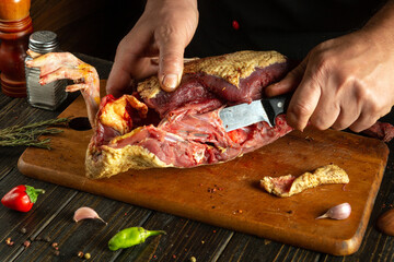 Cutting up a raw duck carcass on the kitchen counter before cooking. A chef holds a knife to cut the bird into small pieces before roasting. The cook prepares the duck
