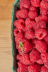 delicious fresh raw red raspberries in natural eco-friendly packaging in a green cardboard basket on a wooden table close-up. harvest. healthy food. diet. summer. vitamins